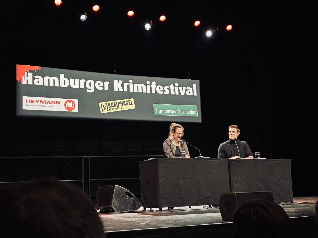 Autor Constantin Schreiber und Moderatorin Maike Schiller sitzen auf der Bühne der Hamburger Krimifestspiele 2024.