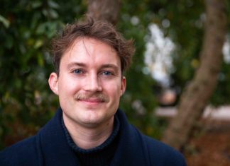 „Ich bin wütend, dass ich Demokraten oder Republikaner wählen muss” Dylan Johnson steht vor einem Baum an der Alster. Er guckt genau in die Kamera. Er hat einen Schnauzer und hellblaue Augen.