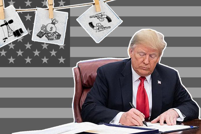 Trump sitzt am Schreibtisch. Im Hintergrund ist die US-Flagge zu sehen.