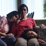 „Die Saat des heiligen Feigenbaums“ oscarnominiert Drei Frauen sitzen gemeinsam auf einem Sofa. Eine Frau sitzt in der Mitte, die beiden Mädchen rechts und links von ihr lehnen ihre Köpfe an. Der Film ist für die Oscars nominiert.