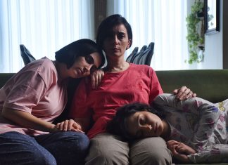 „Die Saat des heiligen Feigenbaums“ oscarnominiert Drei Frauen sitzen gemeinsam auf einem Sofa. Eine Frau sitzt in der Mitte, die beiden Mädchen rechts und links von ihr lehnen ihre Köpfe an. Der Film ist für die Oscars nominiert.