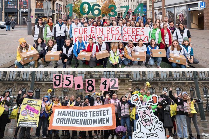 Volksentscheide auf der Kippe: Viele Menschen vom Volksentscheid Hamburg testet Grundeinkommen und vom Volksentscheid Zukunftsentscheid stehen vor dem Hamburger Rathaus. Sie halten Zahlen in die Höhe.