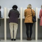 Wie gefährlich sind KI-Fakes im Wahlkampf? Vier Menschen stehen nebeneinander in Wahlkabinen.