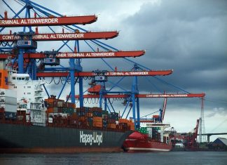 Landstrom wird am Hafen wenig genutzt Ein Bild vom Hamburger Hafen. Der Himmel ist grau-blau und stark bewölkt. Ein Containerschiff liegt vor rot-blauen Hafenkranen. Hier gibt es seit Mai Landstrom.