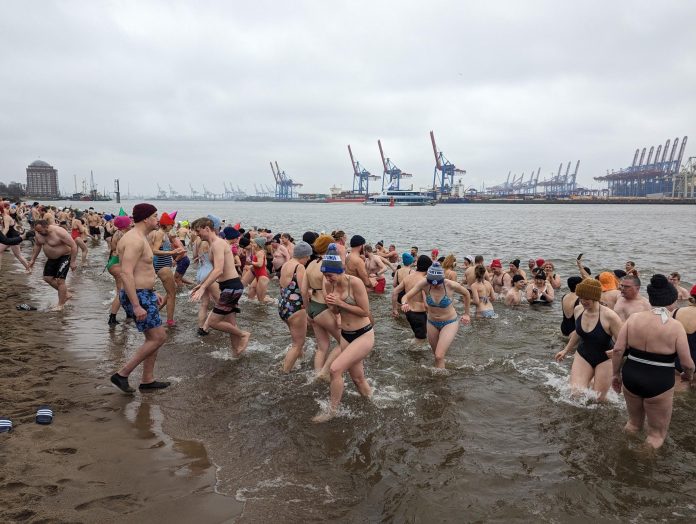 Zahlreiche Menschen gehen in der Elbe Eisbaden. Im Hintergrund ist ein Teil des Hafens zu sehen. Foto: Eisbademeisters Hamburg