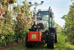 Ein Trecker mit einer Sensorbox steht im Zentrum des Fotos. Links und rechts befinden sich Apfelbäume. Foto: SAMSON-Projekt