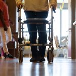 Rückkauf von Pflegeeinrichtungen Symbolbild: Ein Pflegefall läuft mit Rollator einen Gang entlang in einer Pflegeeinrichtung. Foto: Marijan Murat/dpa.
