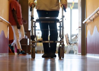 Rückkauf von Pflegeeinrichtungen Symbolbild: Ein Pflegefall läuft mit Rollator einen Gang entlang in einer Pflegeeinrichtung. Foto: Marijan Murat/dpa.