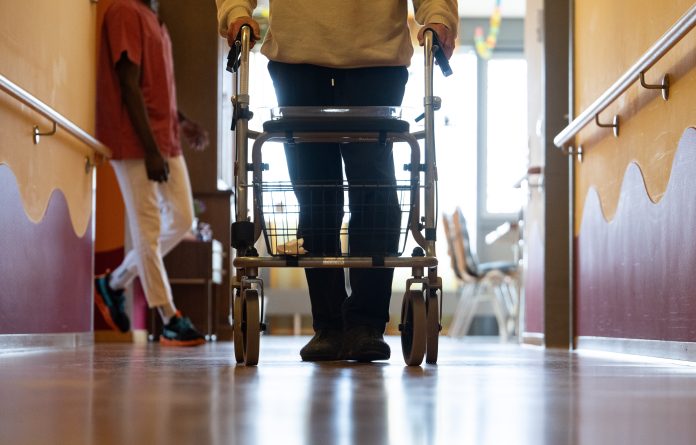 Symbolbild: Ein Pflegefall läuft mit Rollator einen Gang entlang in einer Pflegeeinrichtung. Foto: Marijan Murat/dpa.