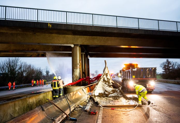 Einsatzkräfte stehen auf der Autobahn 1 nach einem Unfall an einer Brücke. Ein Lastwagen ist wegen eines geplatzten Reifens gegen die Brücke geprallt, dabei wurden 18 Menschen in anderen Fahrzeugen wurden leicht verletzt.