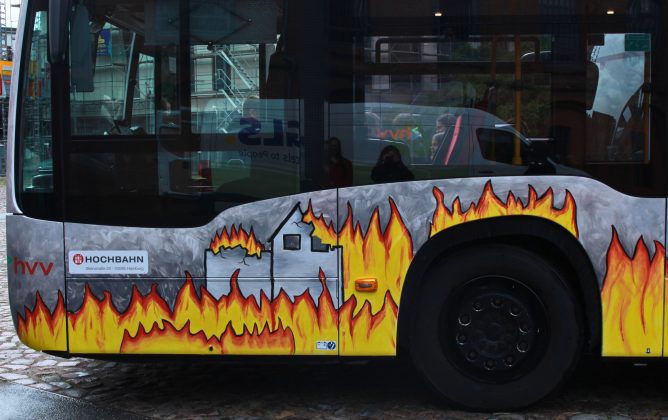 Auf dem Bus sieht man ein brennendes Haus und viel Feuer drumherum.