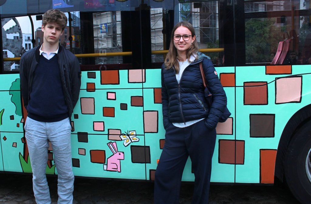 Ein Junge und ein Mädchen stehen lächelnd vor dem angemalten HVV-Bus.