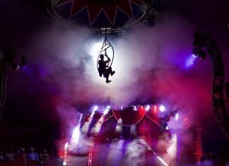 Zirkusleben ungeschminkt Artistin schwebt in einem Reifen über der Manege im Zirkuszelt.