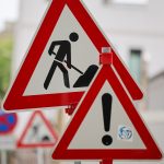 Bauarbeiten an der Hamburger Elbgaustraße bis 2027 Zwei Baustellenschilder stehen im Vordergrund. Im Hintergrund ist verschwommmen eine Straße zu sehen.