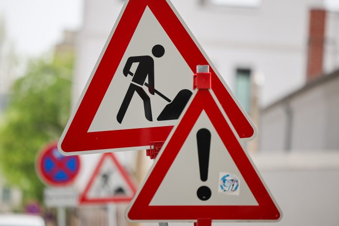 Zwei Baustellenschilder stehen im Vordergrund. Im Hintergrund ist verschwommmen eine Straße zu sehen.