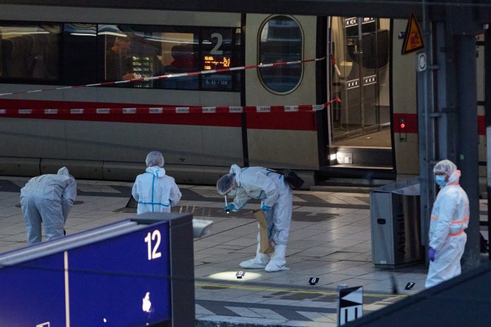Ermittler in Schutzanzügen sichern Spuren an einem abgesperrten Bahnsteig vor einem ICE-Zug in einem Bahnhof. Der Bereich ist mit rot-weißem Band abgesperrt.
