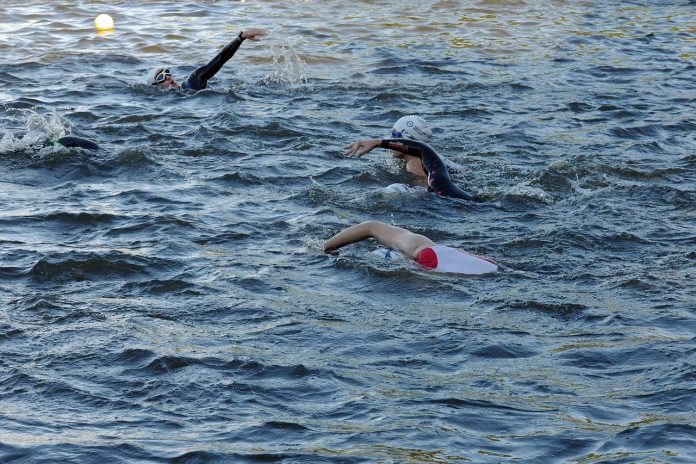 Fünf Personen mit Schwimmkappen und Schwimmbrillen schwimmen nebeneinander in der Alster.