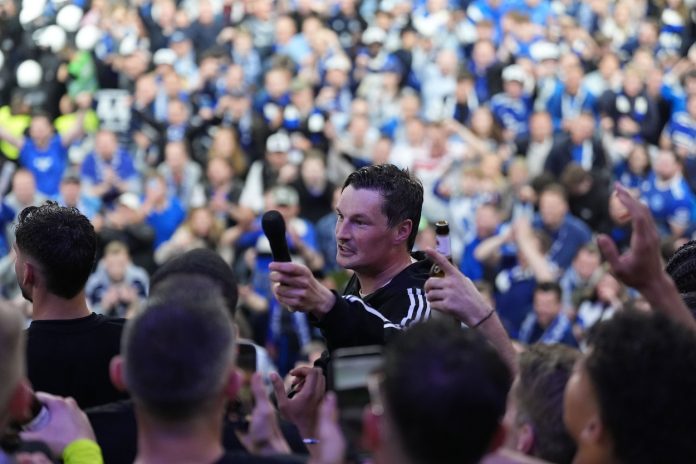 HSV Trainer Merlin Polzin Auf dem Bild ist HSV-Trainer Merlin Polzin zu sehen, der inmitten der Fans steht und ihnen ein Mikrofon entgegenhält.