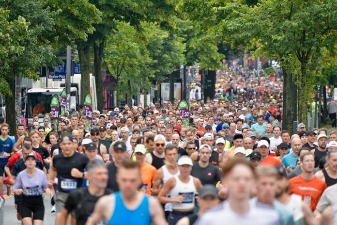 Mehrere Menschen laufen einen Halbmarathon. Sie laufen eine Straße entlang und tragen Sportkleidung.