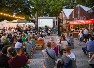 Altonale 2025: Kulturfestival startet am Freitag Viele Menschen sitzen draußen auf Bänken und an Tischen. Sie schauen in Richtung einer großen Leinwand.