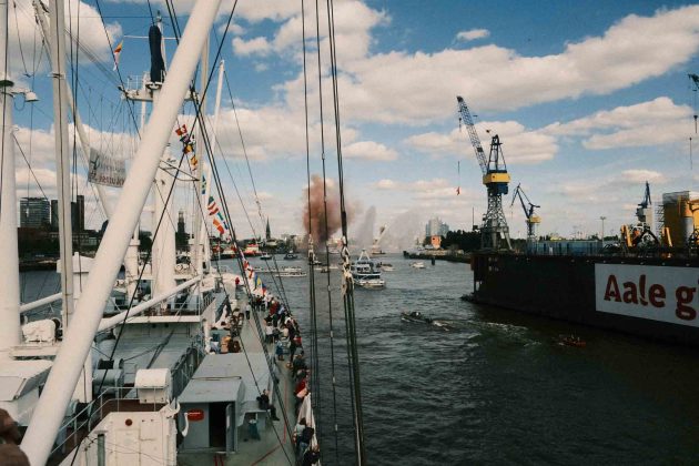 Die Cap San Diego fährt durch den vollen Hamburger Hafen. Das Schlepperballet läuft im Hintergrund und von einem Schiff wird ein Feuerwerk gezündet.
