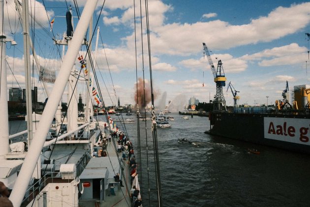 Die Cap San Diego fährt durch den vollen Hamburger Hafen. Das Schlepperballet läuft im Hintergrund und von einem Schiff wird ein Feuerwerk gezündet.