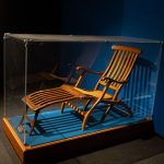 Ein brauner Sonnenstuhl in einer Vitrine aus Glas.