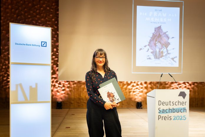 Die Gewinnerin des Deutschen Sachbuchpreises steht mit Buch und Urkunde in der Hand auf einer Bühne