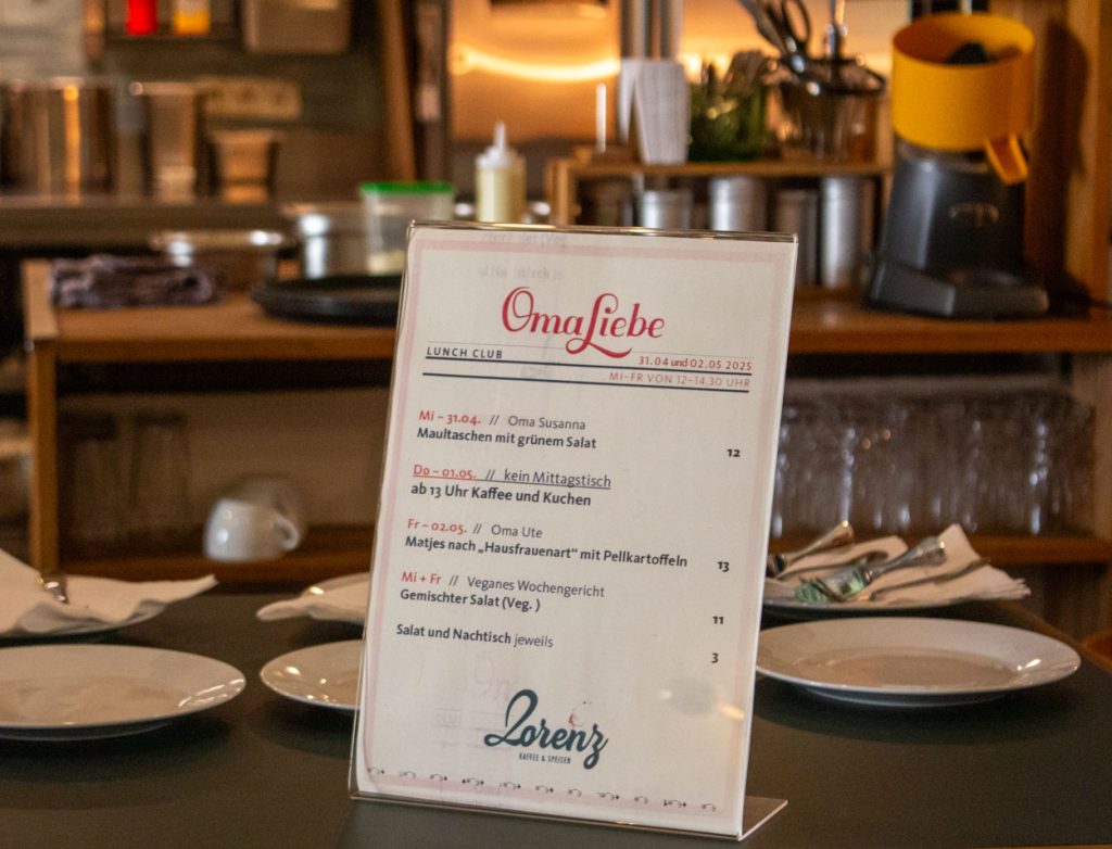 Die Speisekarte des Oma Liebe Lunch Pop-Up-Restaurants steht als Austeller auf dem Tresen. Es ist eine weiße Karte mit schwarzer Schrift, auf der die Wochengerichte des Oma Liebe Lunch Pop-Up-Restaurants zu lesen sind.