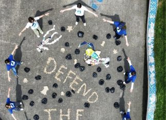 Kippen sammeln: Kunst aus Zigarettenstummeln Die Teilnehmer*innen stehen im Kreis um das Kunstwerk aus Müll. Aus Zigarettenstummeln steht geschrieben "Defend the Deep".