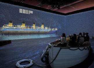 Virtuell an Bord der Titanic 360-Grad-Lichtprojektion in einem großen Raum. Sie zeigt die Titanic. In der Mitte steht ein Rettungsschiff, in dem sich Besucher*innen befinden.