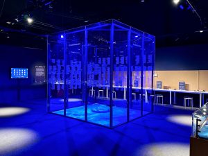 Der Raum ist blau beleuchtet und zeigt einen großen Glaskasten mit Namen der Passagier*innen eingeteilt in Klasse und Lost oder Saved.