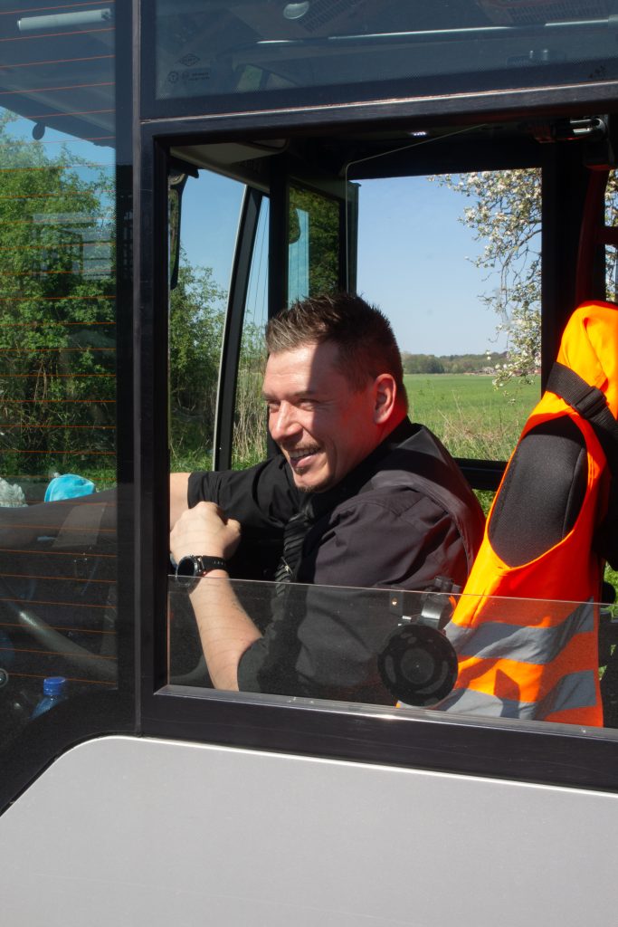 Ein lächelnder Busfahrer sitzt in der Fahrerkabine eines Busses.