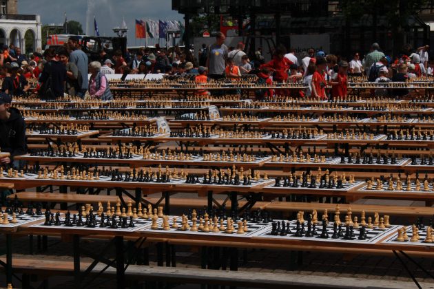Dutzende Schachbretter stehen mit Figuren auf langen Reihen mit Bierbänken. Im Hintergrund spielen Menschen an den Brettern und man sieht die Alsterfontäne.
