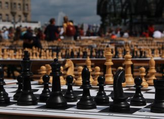Größtes Schul-Schachturnier der Welt auf dem Rathausmarkt Schachfiguren im Vordergrund auf einem Schachbrett. Im Hintergrund sind weitere Tafeln voller Schachfiguren mit Menschen unter freiem Himmel.