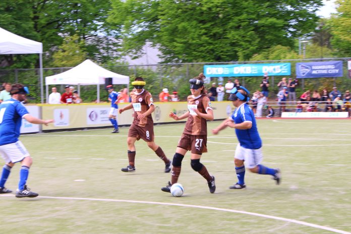 Vier Spieler*innen beim Blindenfußball auf dem Feld.