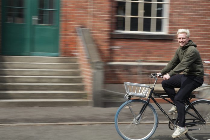 Ein junger Mann auf dem Fahrrad. Im Hintergrund ist ein Steingebäude, Bewegungsunschärfe