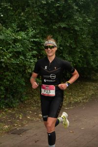 Triathletin Konczalla im schwarzen Triathlonanzug, Sonnenbrille, bunten Socken und gelben Socken läuft beim Hamburg Ironman durch den Alsterpark.