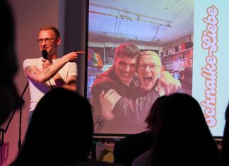 „Love at First Slide”: Pitch your Best Friend Ein junger Mann steht auf einer Bühne vor Publikum. Er deutet auf eine Präsentation neben ihm, die ein Foto von ihm und seinem besten Freund Arm in Arm zeigt.