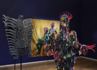 „Mehr als ein paar Glitzerpullis und ein Zauberstab“ bunte und glitzernde Kleidung in einem Raum ausgestellt