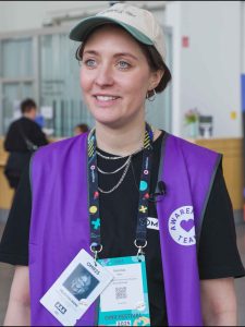 Felicitas Niere ist die Leiterin des Awareness-Teams auf der OMR. Sie trägt eine lila Weste, die das Awareness-Team kennzeichnet, trägt eine Cap und lächelt in die Kamera.