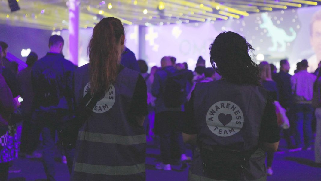 Zwei Mitarbeitende des OMR Awareness-Teams stehen mit dem Rücken zur Kamera. Sie schauen auf eine Menschenmasse, im Hintergrund ist eine Bühne zu sehen.