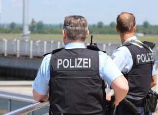 Jimi Blue Ochsenknecht am Hamburger Flughafen verhaftet Zwei Polizisten von hinten, während sie auf das Rollfeld eines Flughafens blicken.