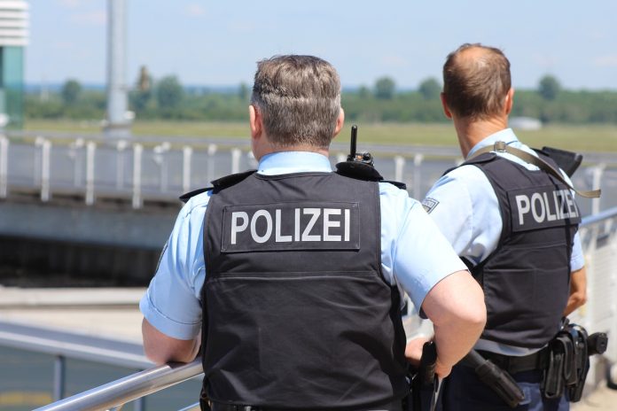 Ochsenknecht_Flughafen_Hamburg Zwei Polizisten von hinten, während sie auf das Rollfeld eines Flughafens blicken.