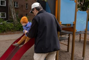 Ein kleines Mädchen rutscht, ein Mann steht beschützend daneben.