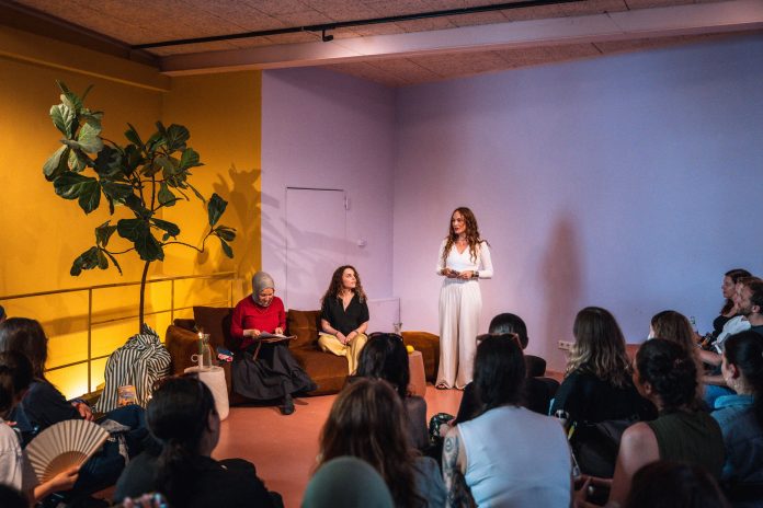 Kübra Gümüsay und Alena Jabarine sitzen auf der Couch, während Jessica die Lesung vor dem Publikum eröffnet.