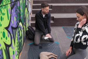 Ein Hundetrainer auf den Knien gestickuliert, wie man einen Hund wiederbelebt.