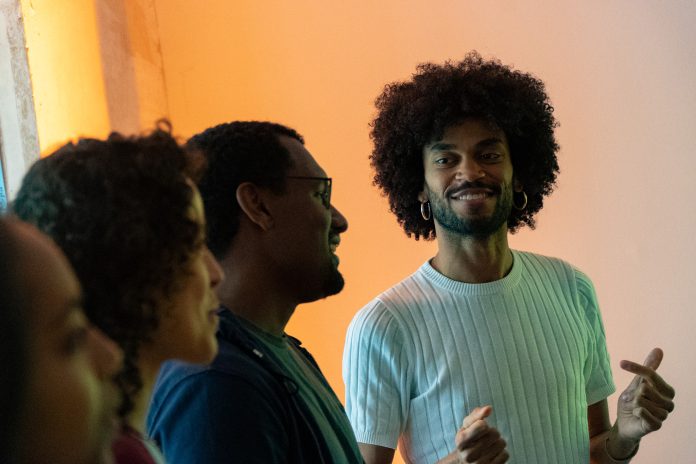 FAYIM schaut stolz auf drei Workshop-Teilnehmer*innen und lächelt dabei. Die Teilnehmer*innen singen.