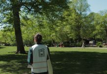 Streitfall Außenwerbung: Zwischen Litfaßsäule und LED-Screen Ein Mann im grünen Hemd, mit weißer Warnweste und Jutebeutel läuft durch einen Park. Im Hintergrund sind unscharf zwei Menschen zu sehen, die Federball spielen. Auf dem Rücken der Weste steht "Hamburg Werbefrei"