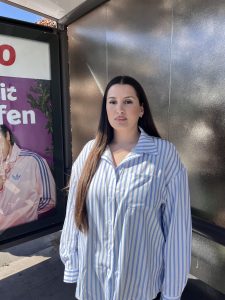 Eine Frau um die 30 steht in einer Bushaltestelle.